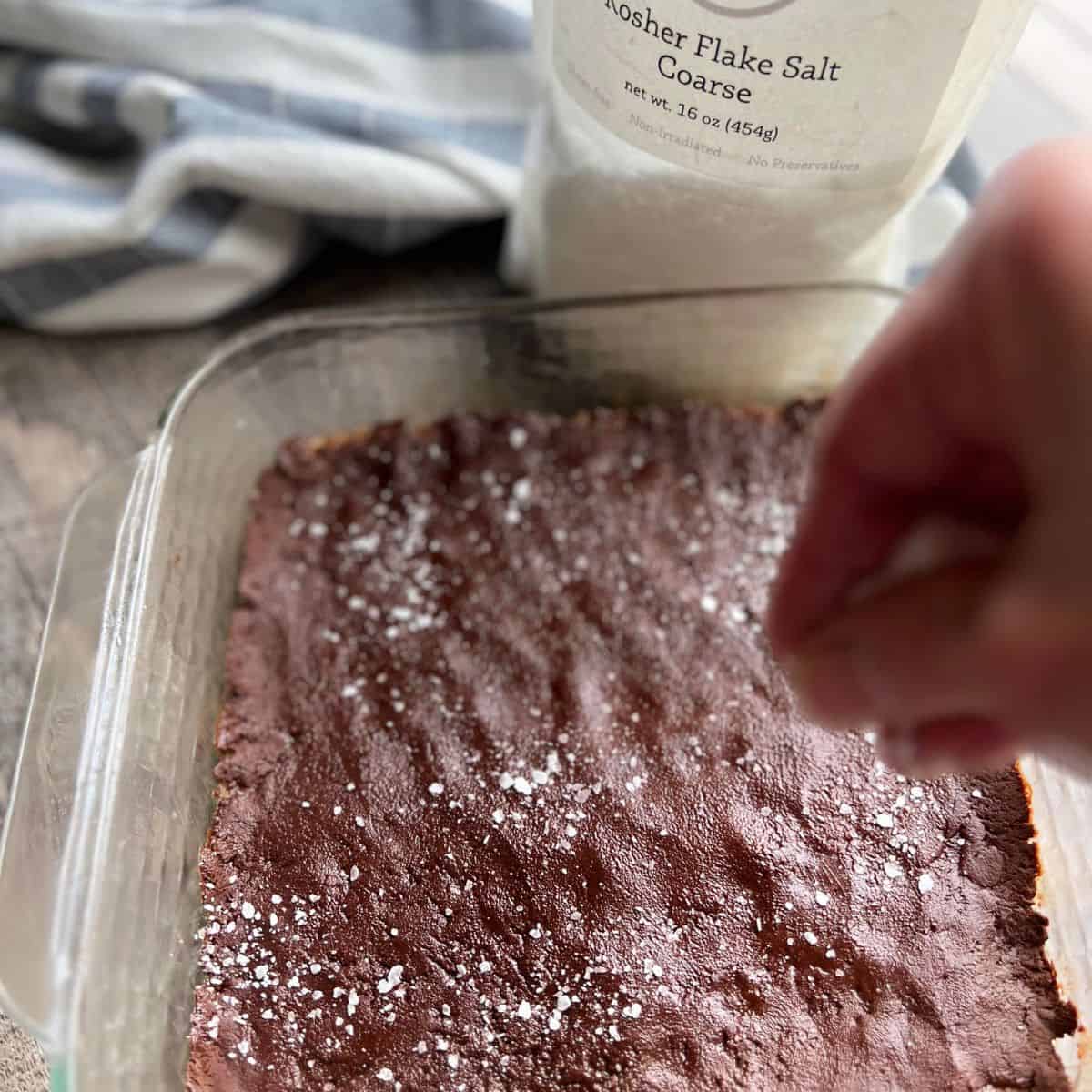 The bars are in an 8x8 glass dish with the chocolate layer on top getting a sprinkle of coarse flake salt before the bars are cut.