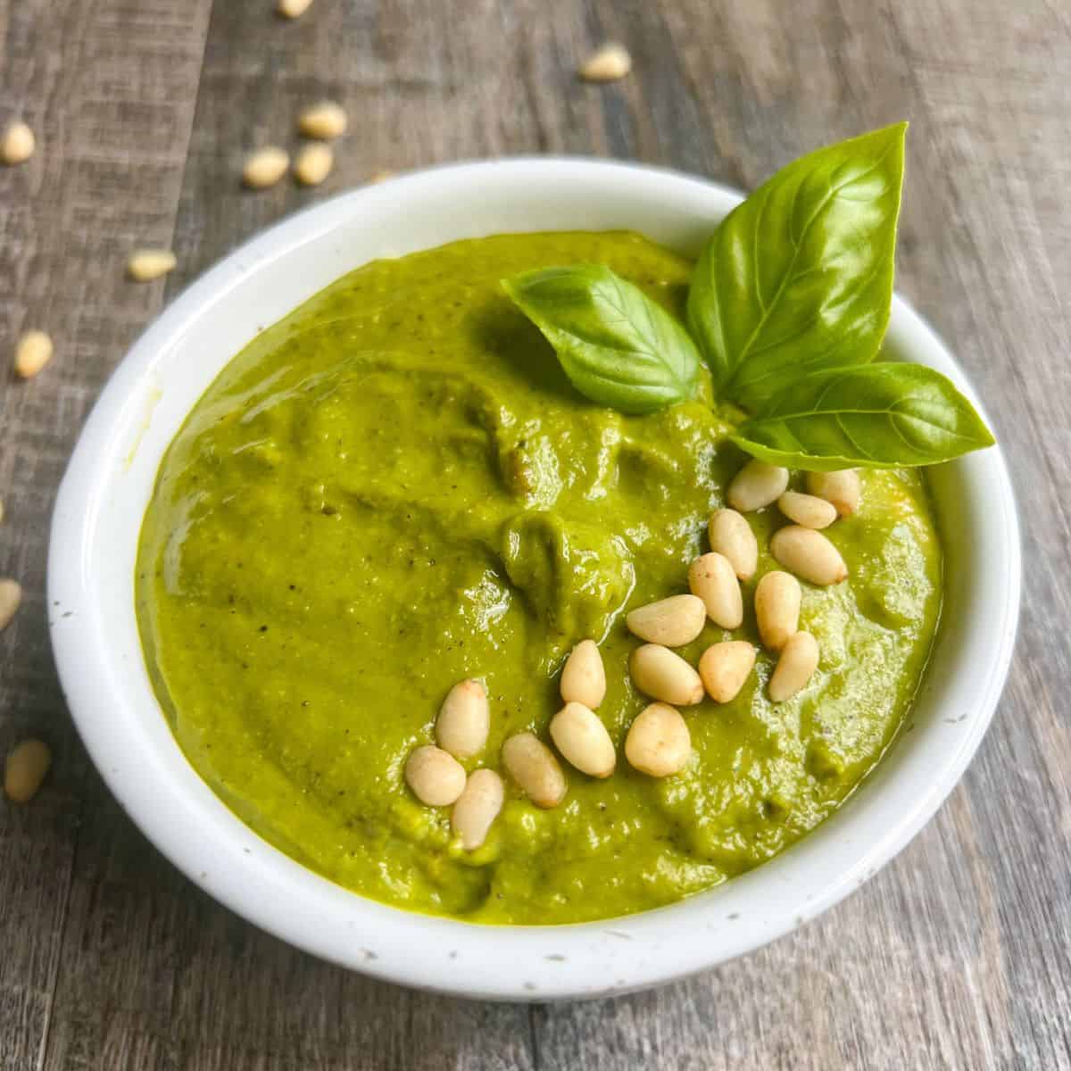 White bowl with Whole30 Pesto garnished with pine nuts and basil leaves.