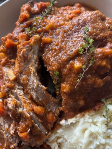 Braised Pork ribs over mashed potatoes in large white round bowl