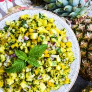 Pineapple salsa in round white bowl with pineapple next to it