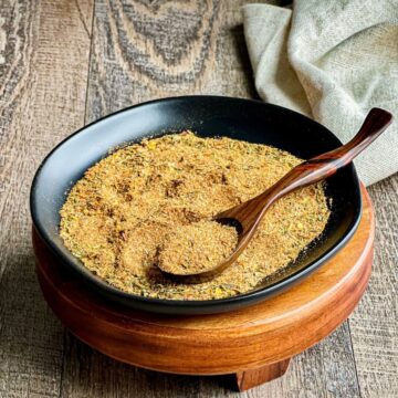 jerk seasoning in black round bowl with wooden spoon on wood pedestal