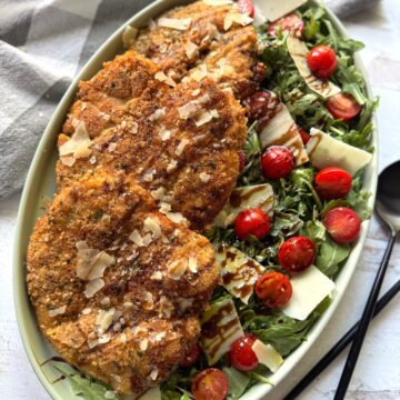 Chicken Milanese on large green oval platter with arugala salad