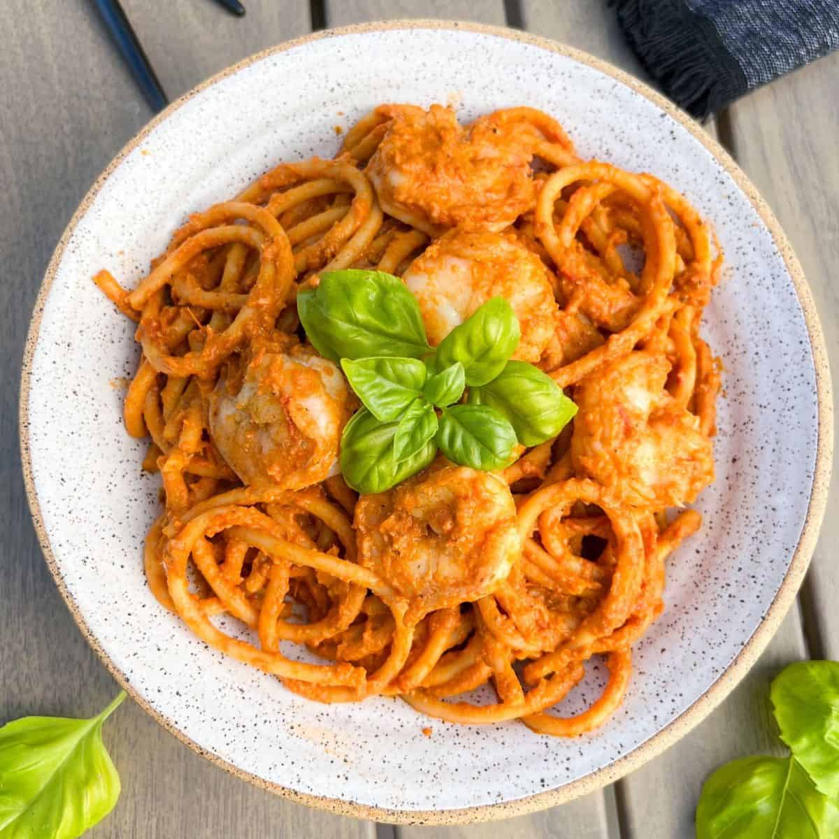 A plate of pasta with tomato sauce and shrimp, garnished with fresh basil leaves, sits on a wooden table.