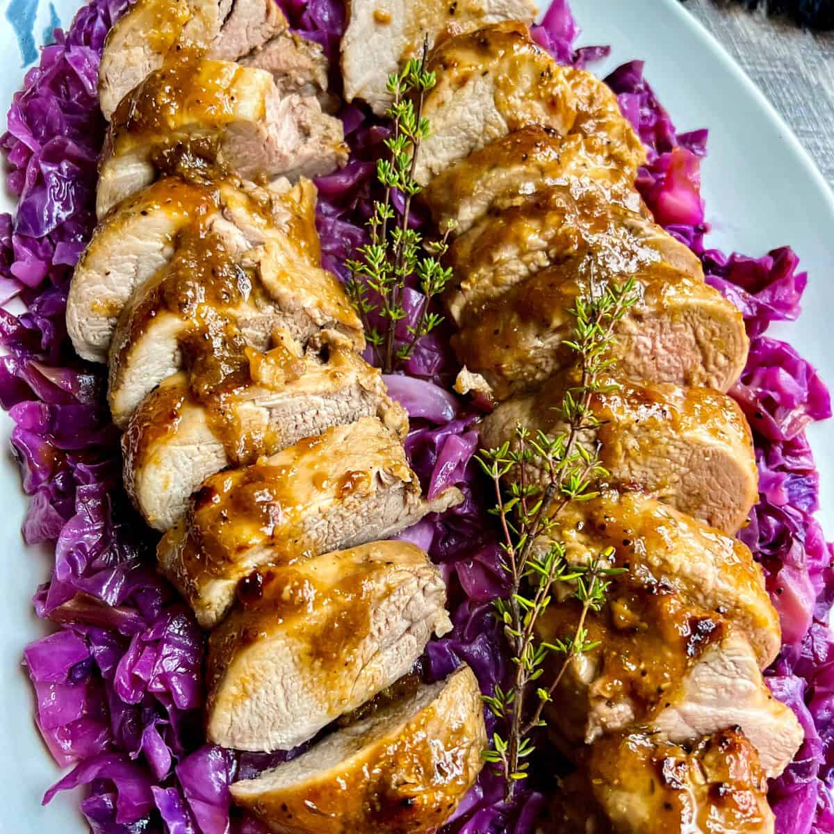 Sliced roasted duck breast with a golden-brown glaze, arranged on a bed of sautéed purple cabbage and garnished with fresh thyme sprigs on a white serving platter.