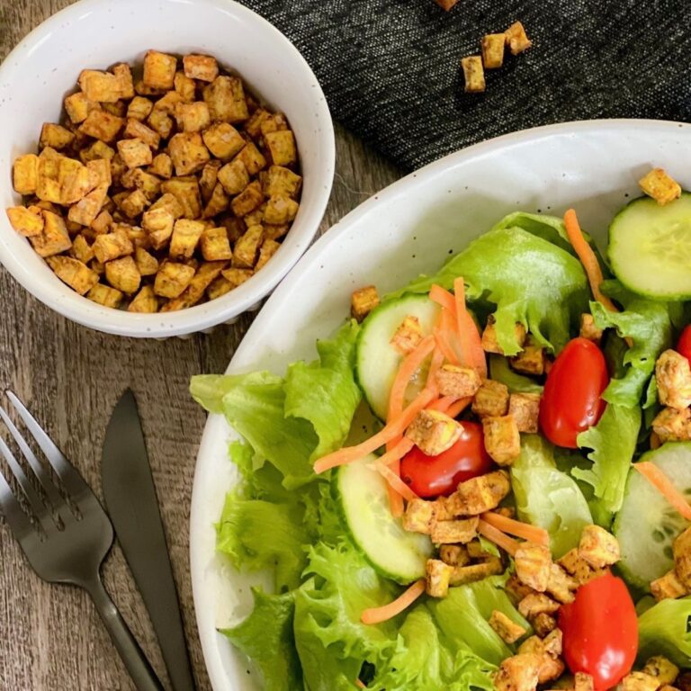 herby plantain croutons over salad with small round bowl full of croutons