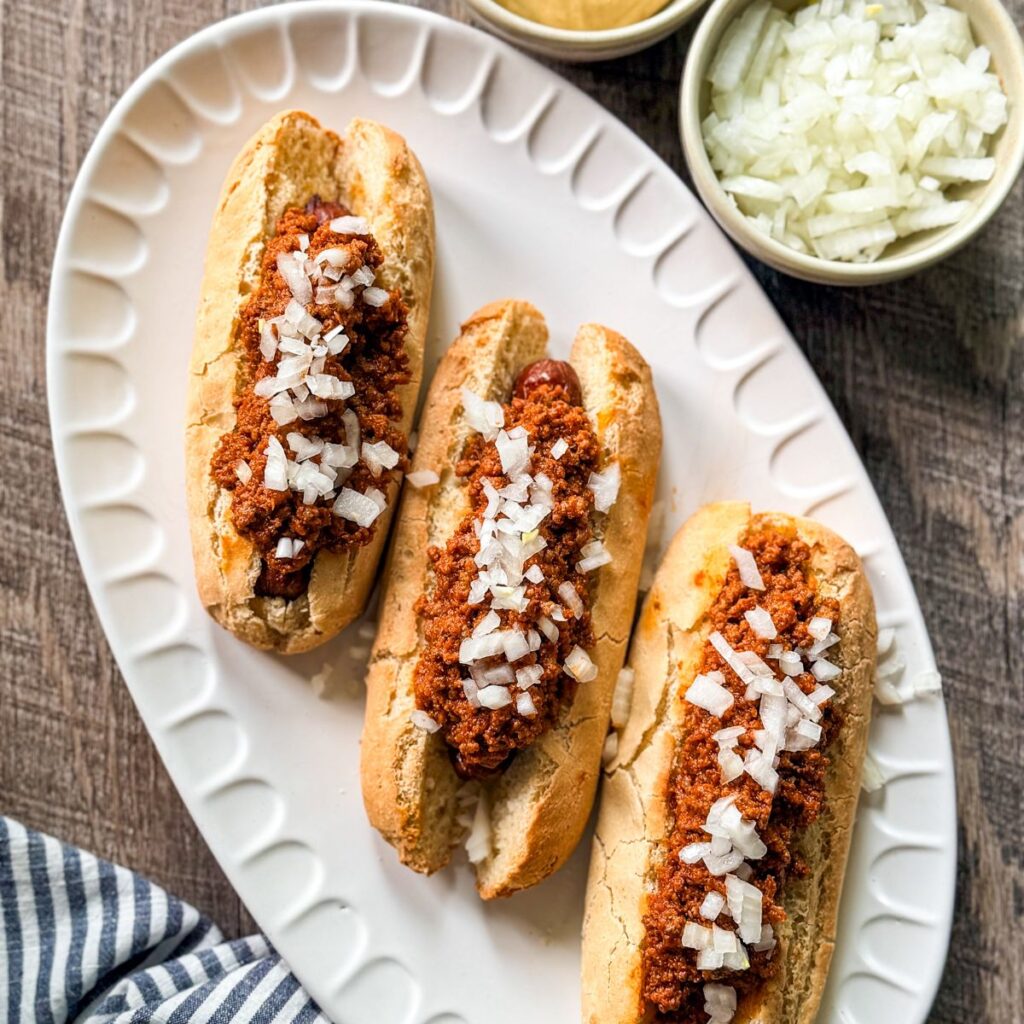 hot dog chili sauce on hot dogs on rolls on oval white platter