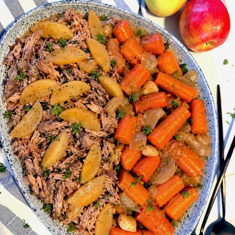 Slow cooker apple cider pork shoulder shredded with apples, carrots, onions, garlic on large blue speckled platter