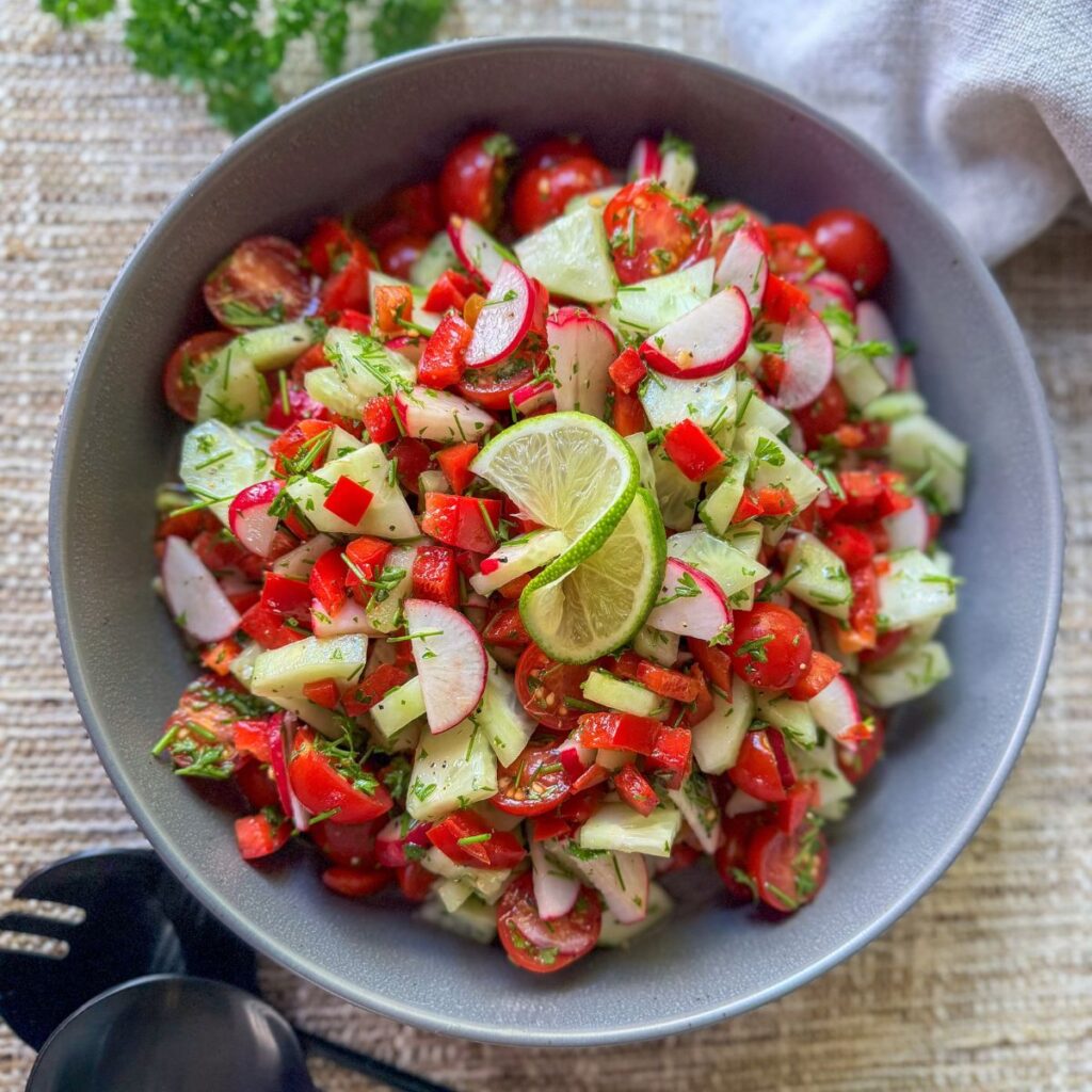 summer crunch salad with cucumbers, cherry tomatoes, radishes, red bell peppers, fresh parsley and fresh chives with lime garnish