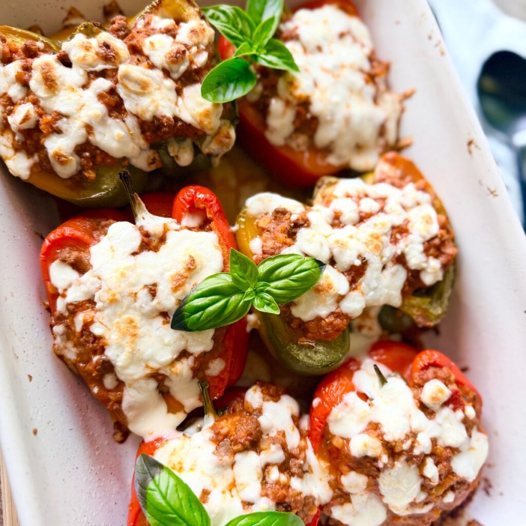 whole30 stuffed peppers green and red cut in half with beef and cauliflower rice stuffing and dairy free mozzarella with basil garnish
